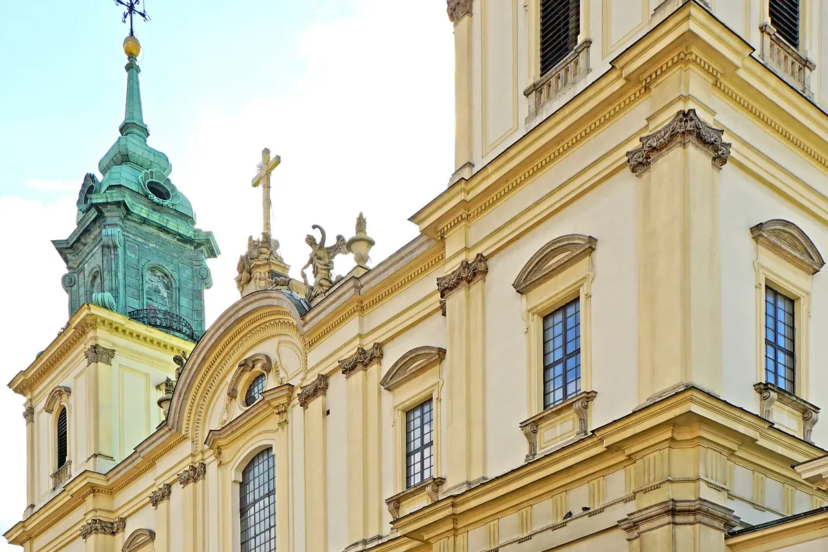 The yellow and cream Baroque façade of Holy Cross Church in Warsaw, with a green copper-roofed tower.