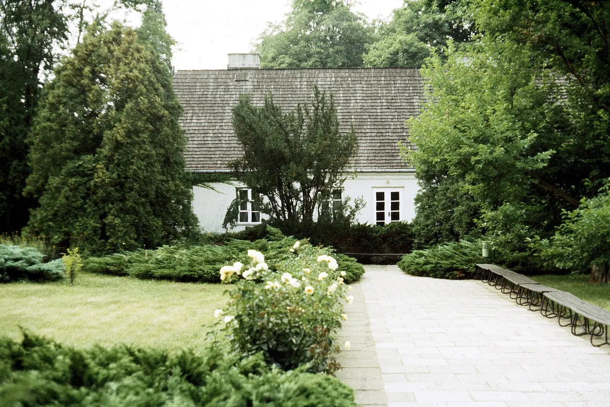 The whitewashed manor house at Żelazowa Wola with a shingle roof, framed by tall evergreens.